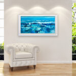 Soft blue ocean oil painting on canvas with rich impasto texture hanging in a modern living room with a white sofa, showing full room decor.